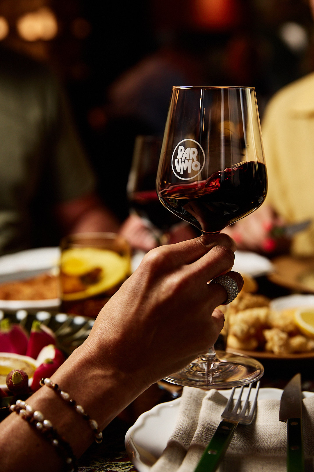 A women's hand swirling a glass of red wine with the logo Bar Vino in clear view.