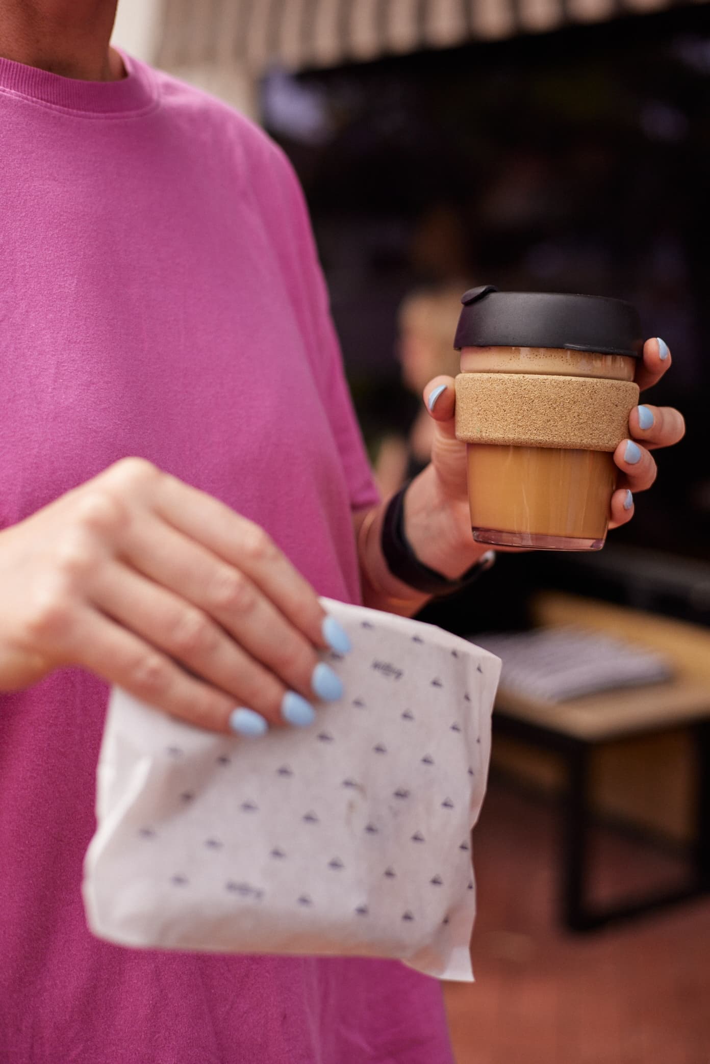 Woman in pink top holding takeaway coffee and food from Willing Coffee in Mount Lawley