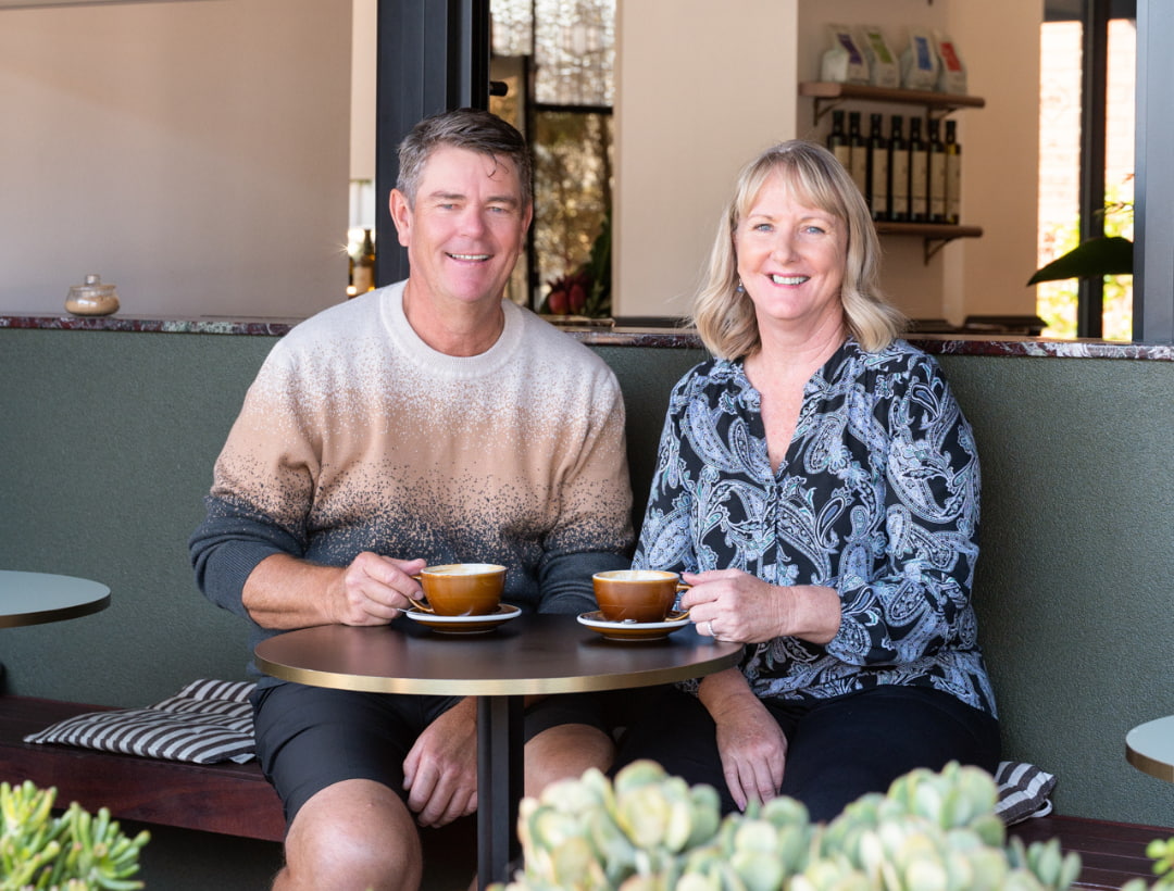 A man and lady smiling at the camera having sitting outside having a coffee at Willing Coffee