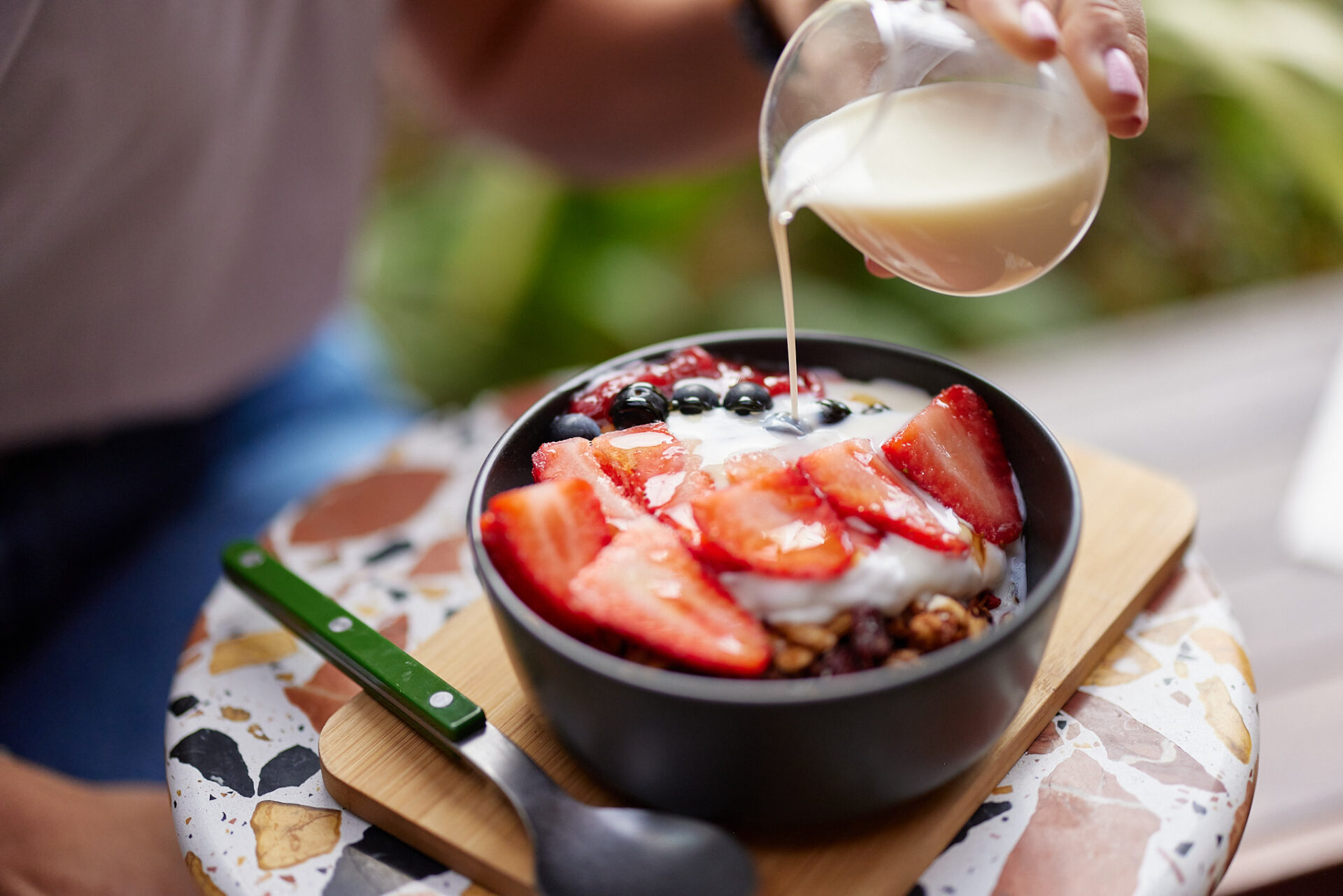 Close up of pouring milk into bowl of fruit yoghurt and museli