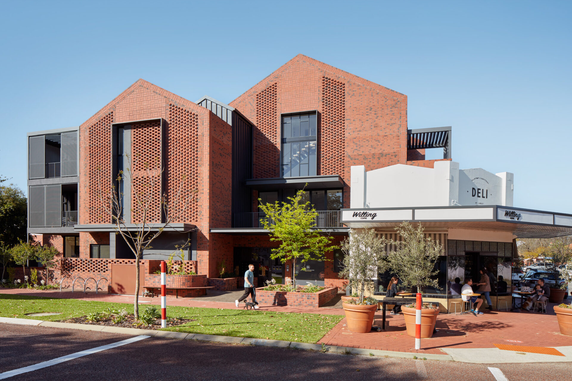 Exterior view of apartment building with busy cafe and coffee shop on the corner, man walking dog on footpath