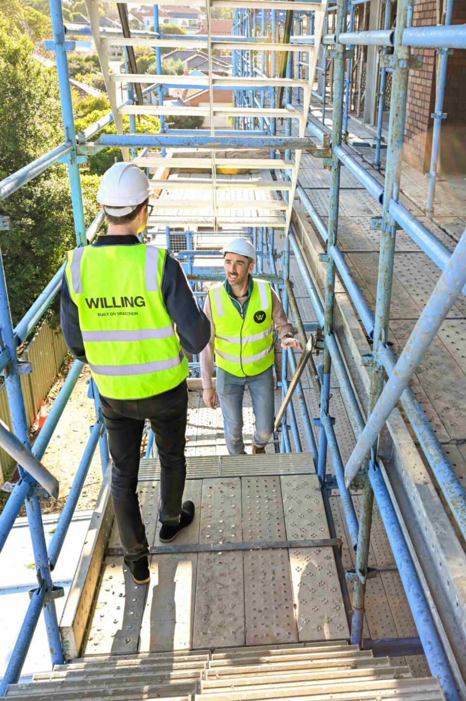 Two Willing Build team members greeting each other on scaffold stairs on at No. 7 Field Street