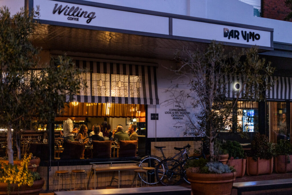 Bar Vino from the street at night looking in through the window to a large group of people eating nad drinking