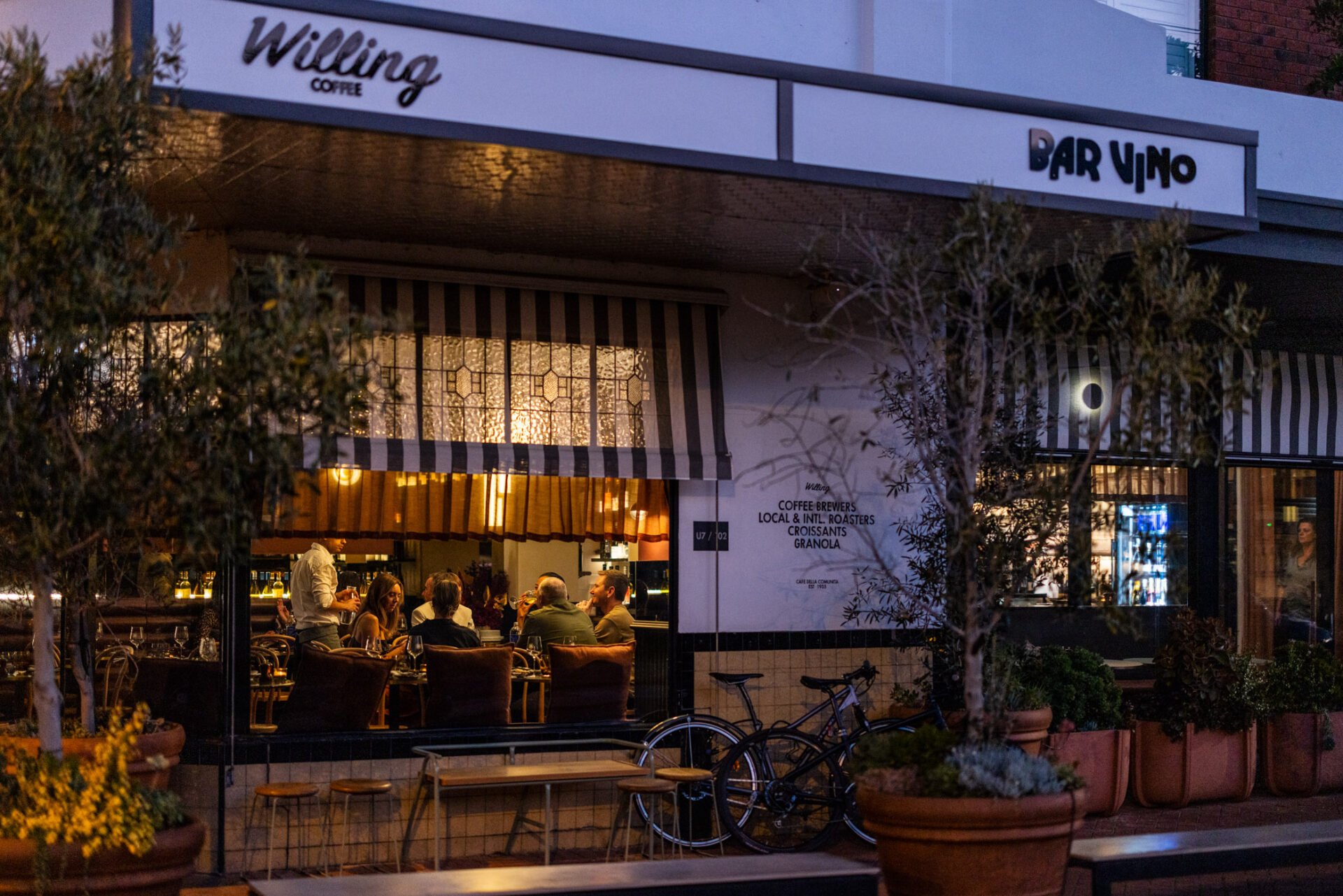 Bar Vino from the street at night looking in through the window to a large group of people eating nad drinking