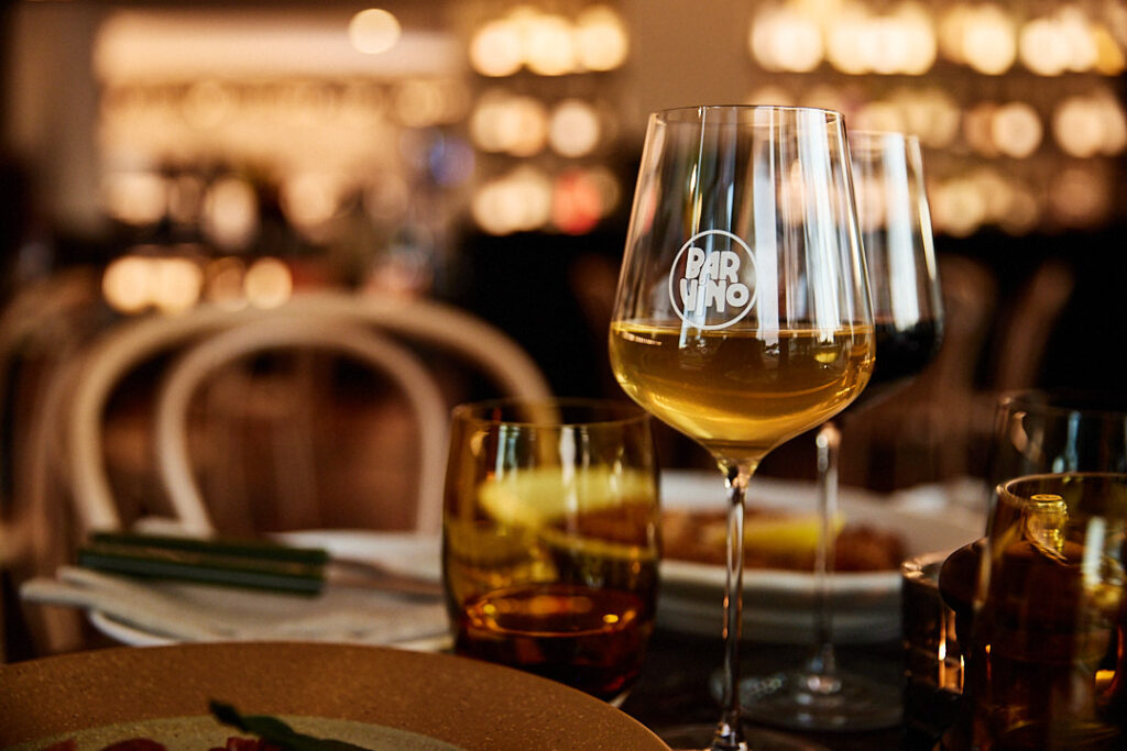 A glass of white wine on the table showing the Bar Vino logo frosted on the outside of the glass.